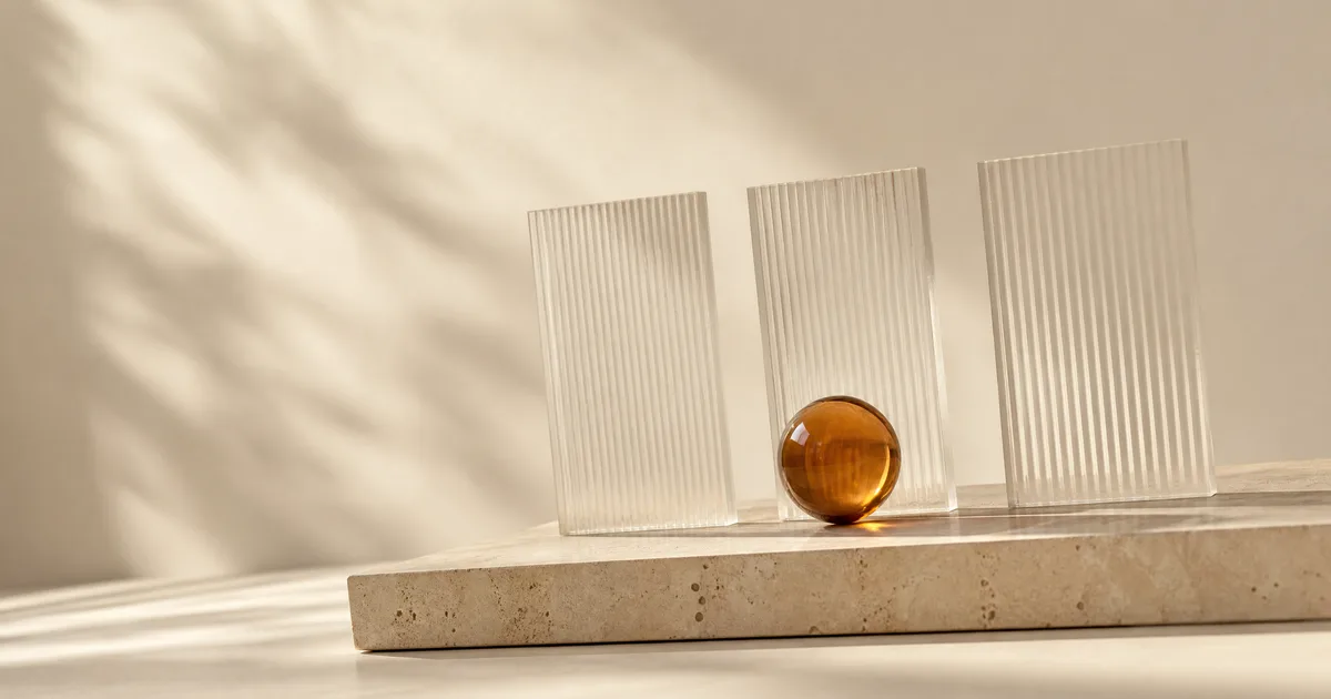 Three upright fluted frosted glass tiles in a row on a travertine plinth with an amber glass sphere in front