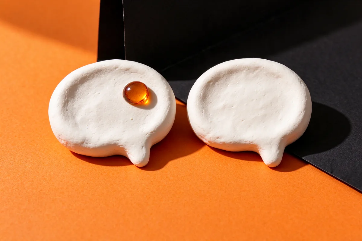 Two white clay speech bubbles side by side, one holding a small amber glass dot, on orange and black paper