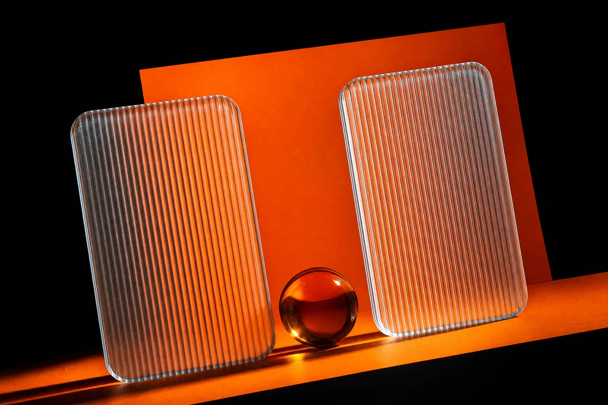 Two tall fluted glass frames side by side with an amber glass sphere between them on black and orange