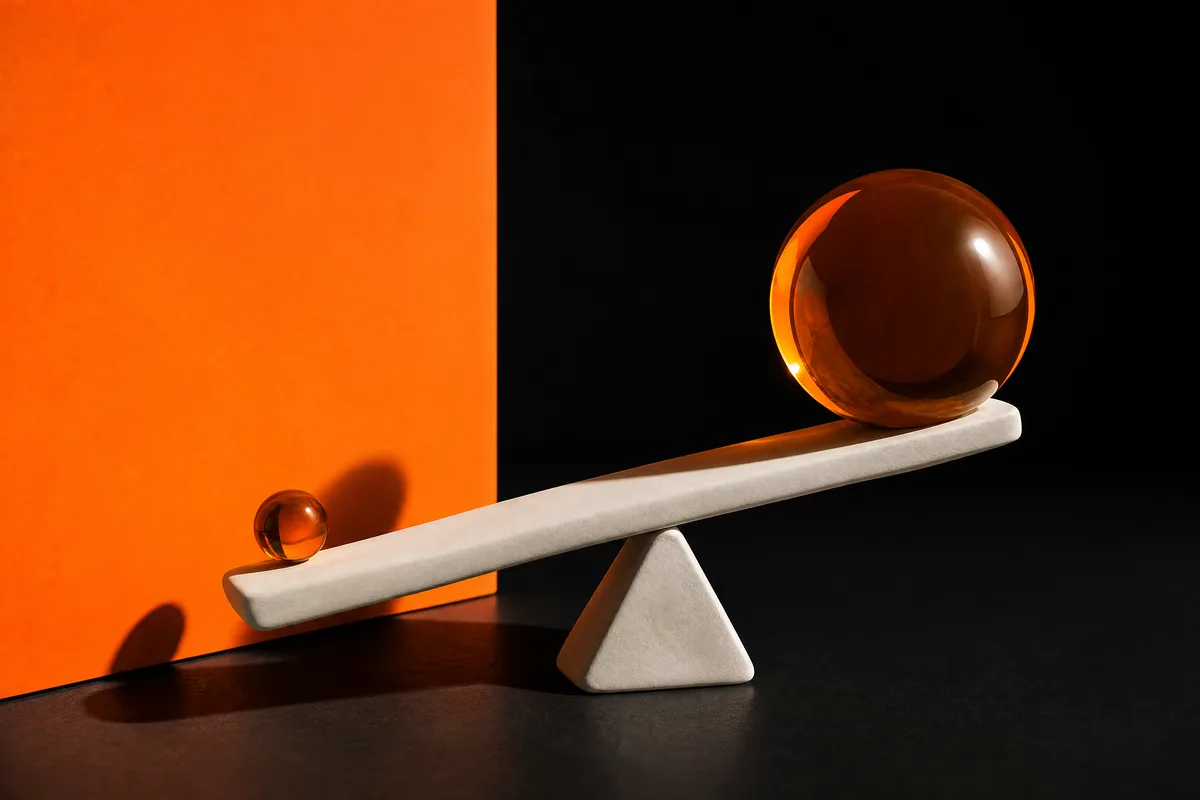 A white clay seesaw where a small amber sphere lifts a much larger sphere, on black and orange