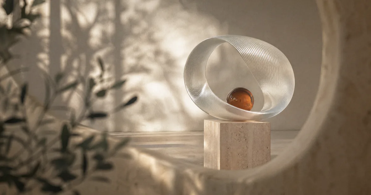 A looping ribbon of fluted frosted glass forming a loop on a travertine plinth with an amber glass sphere inside